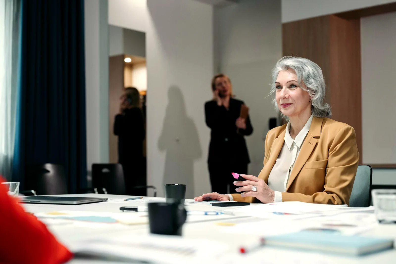 A senior benefits leader in a caramel blazer listens at a conference table