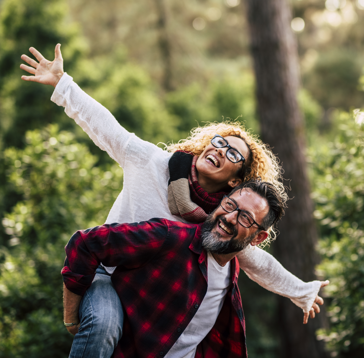 A joyful couple outdoors, the man giving the woman a piggyback ride in a forest