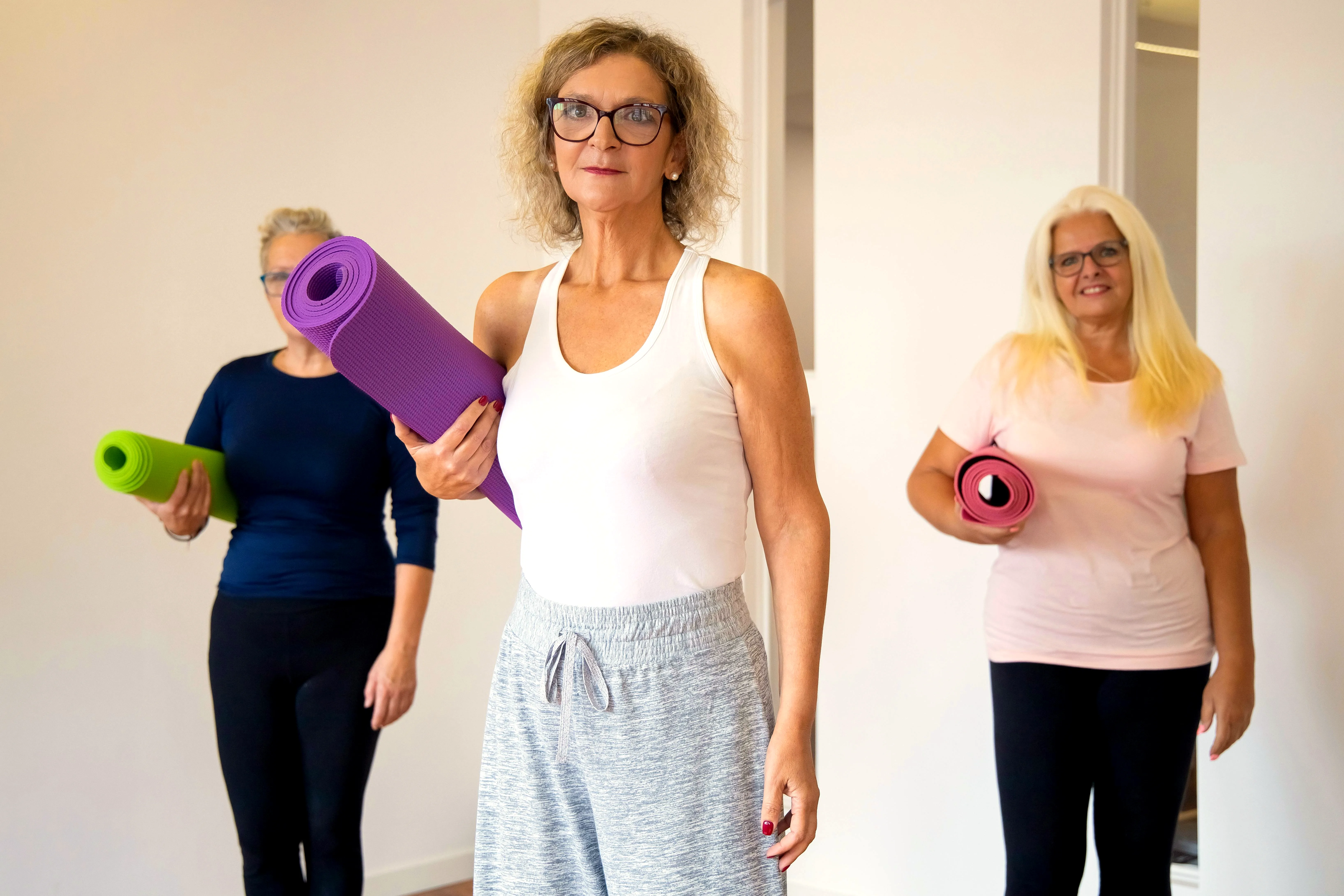 Three older women carrying yoga mats, ready for gentle exercise